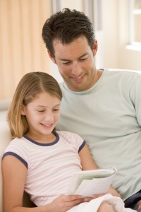 Man and young girl in living room reading book and smiling