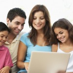 Family Sitting On Sofa At Home With Laptop